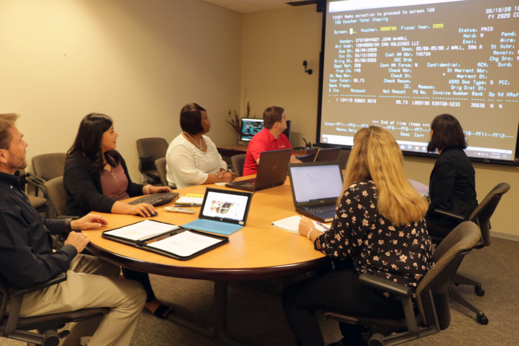 A group of people gathered around a desk as they all inspect data that has been projected on the wall